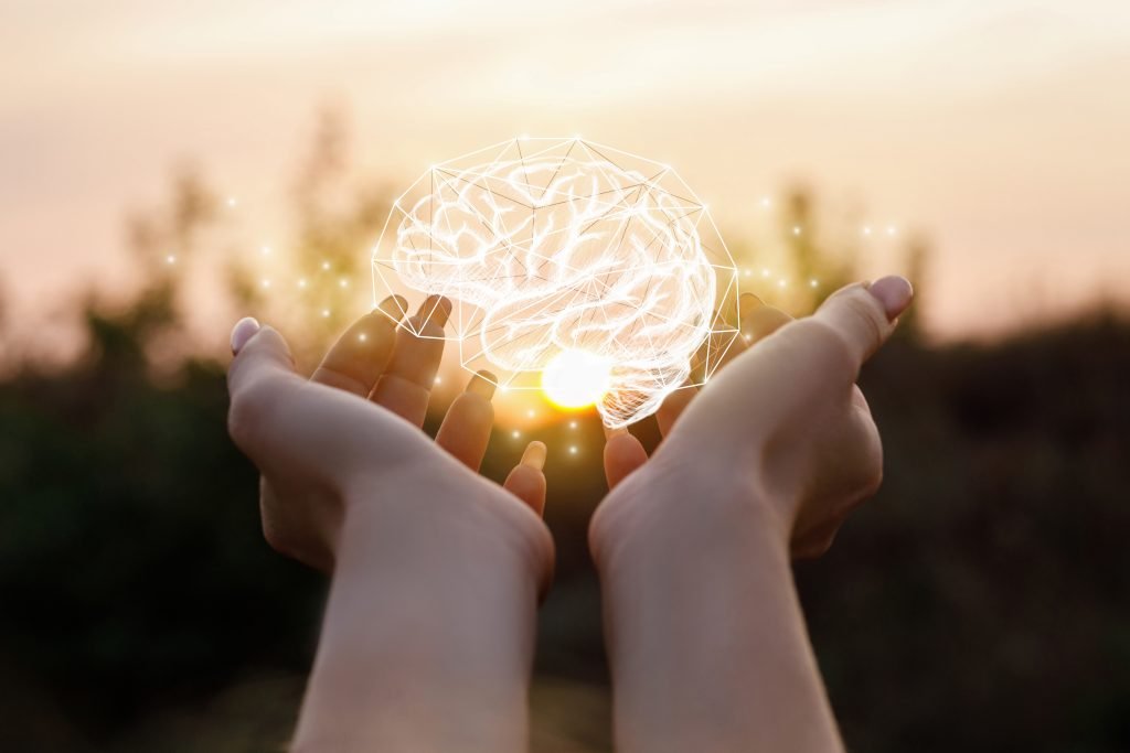 Woman's hand holding up a brain shape against a bright, sunny sky