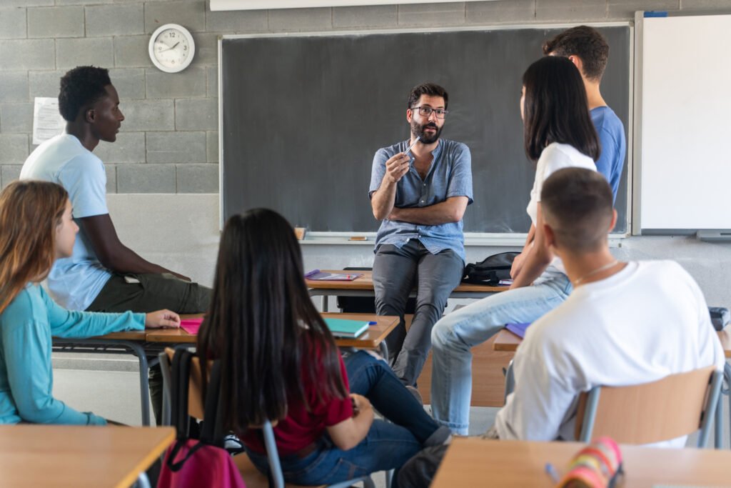 Teacher talking with a group of teenage students seated together in a school classroom