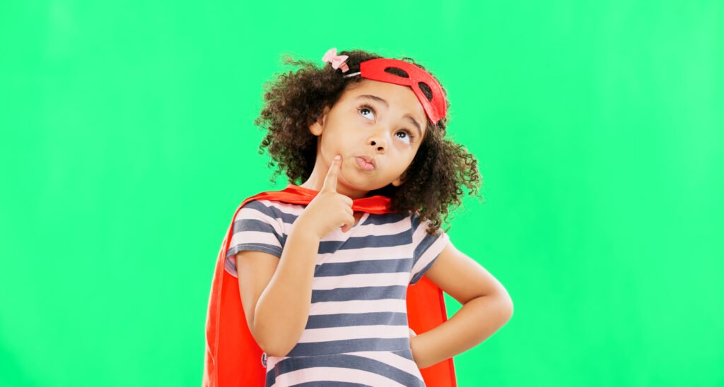 Child in a superhero costume pausing to think, set against a green background
