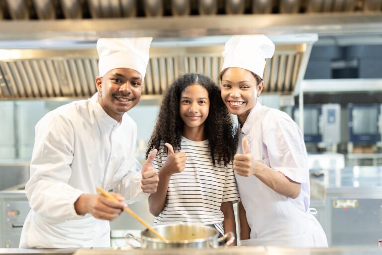 Teen student smiling with two chefs in a commercial kitchen during a career experience